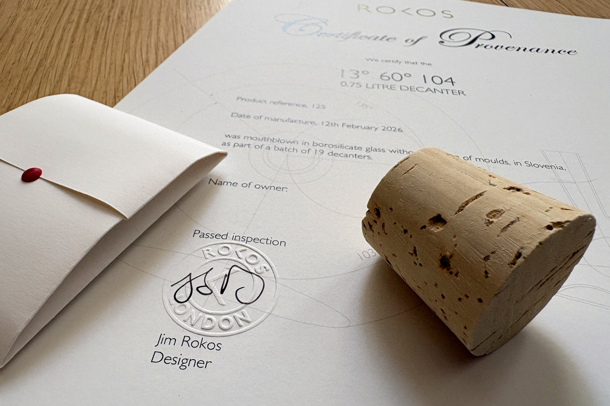 A signed and stamped Certificate of Provenance with an envelope featuring a red wax seal containing decanter cleaning balls, displayed alongside a cork stopper. The certificate includes a space for the owner's name.