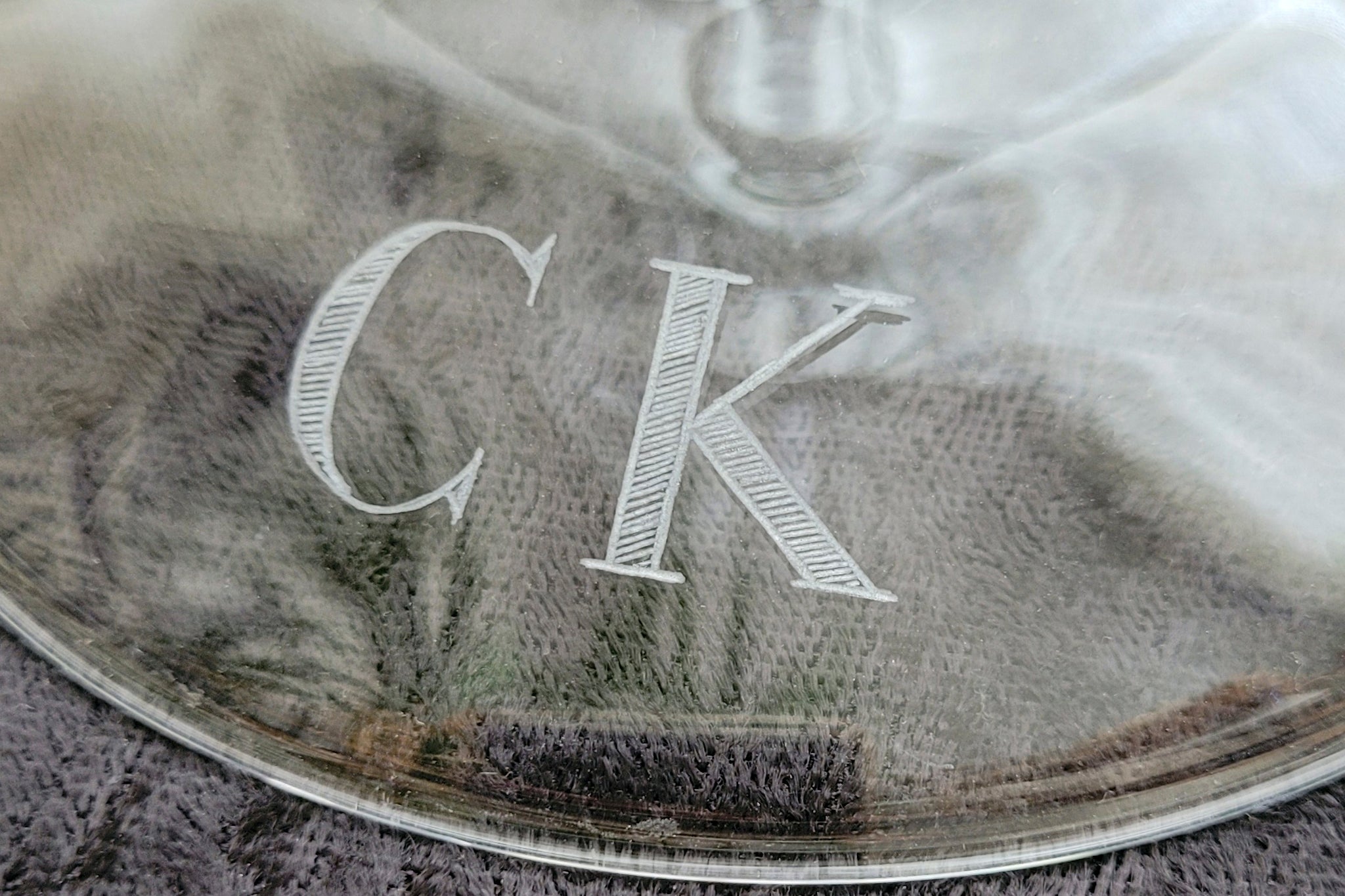Borosilicate glass candleholder base detail with 'CK' initials engraved in capitals in the Bodoni font font.