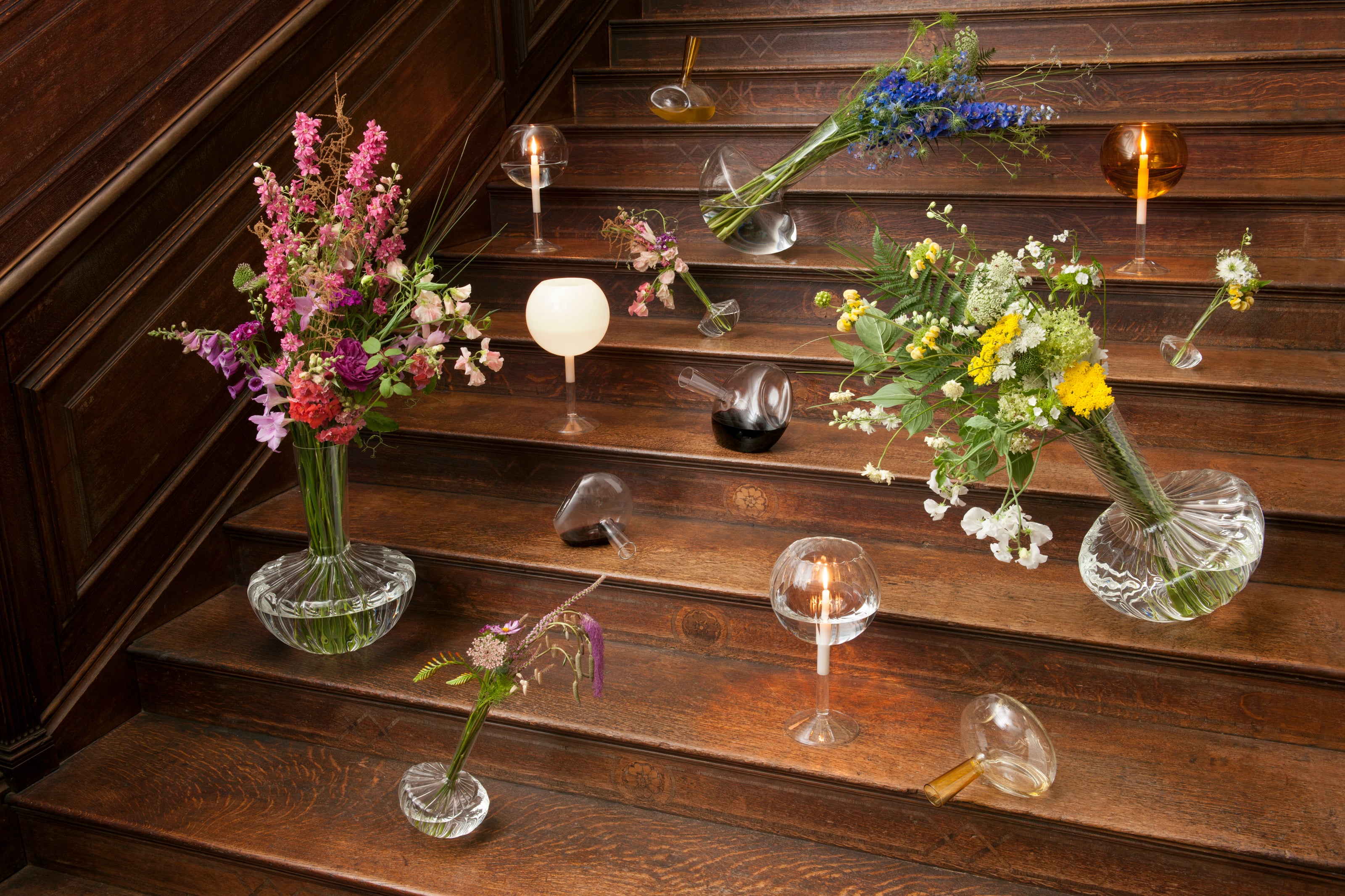 Decorative arrangement of flowers and glass vases on a wooden staircase.