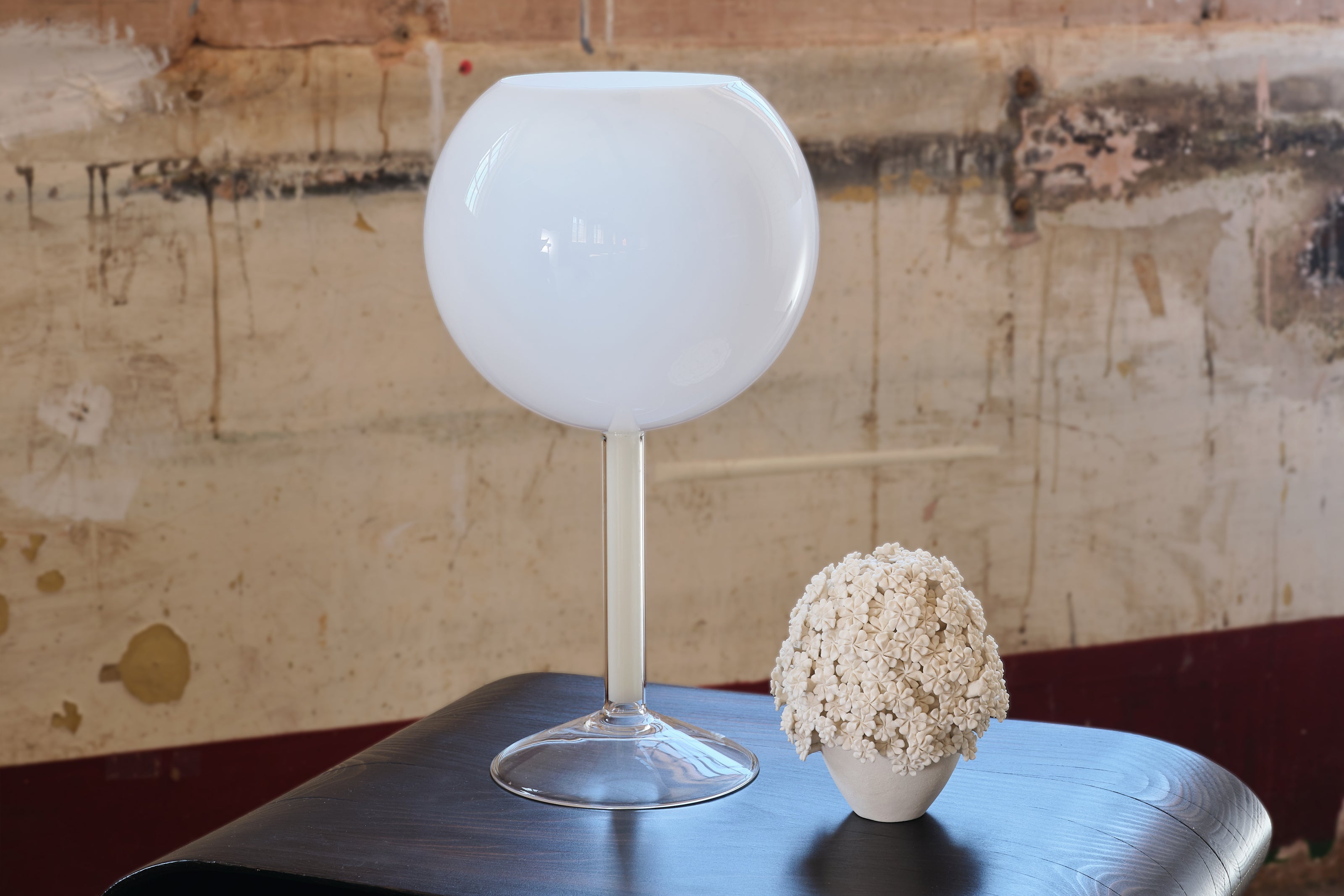 White spherical candleholder on a table with a textured wall background.