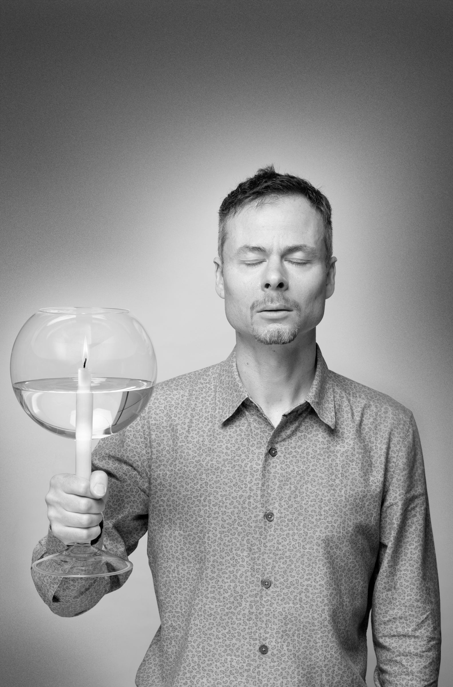 Designer Jim Rokos sleeps, standing and holding a candleholder.