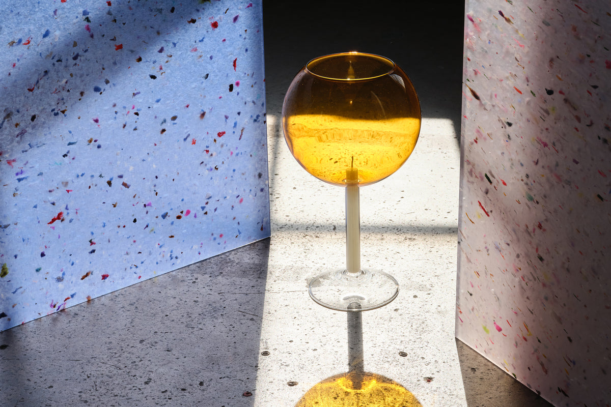 Amber candleholder containing candle sitting on concrete surface. Photograph by Yeshen and styling by Jessica Jung.